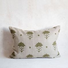 a pillow with green flowers on it sitting against a white wall in front of a wooden frame