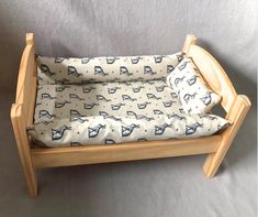 a wooden doll bed with a blue and white cat print cover on the bottom half