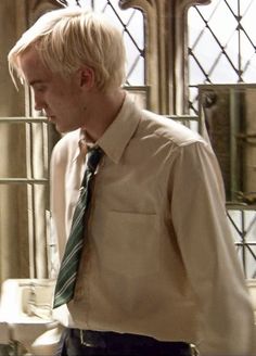 a man with blonde hair wearing a white shirt and green tie standing in front of a sink