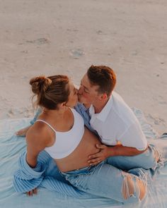 a man and woman kissing on the beach while sitting in the sand with their arms around each other