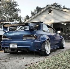 a blue car parked in front of a house with its trunk open and the hood up