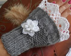 a woman's hand is holding a gray and white knitted wrist warmer