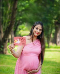 a pregnant woman in a pink dress holding up a sign that says mom to be