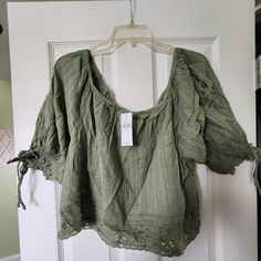 This Olive Green Blouse From American Eagle Outfitters Is A Versatile Addition To Any Wardrobe. With Its Lightweight And Breathable Fabric, This Blouse Is Perfect For All Seasons And Occasions, Whether You're Dressing Up For A Party Or Keeping It Casual While Traveling. The Round Neck And Cap Sleeves, With Tie Details, Add A Touch Of Femininity To The Simple Yet Stylish Design. The Blouse Comes In Size Small And Features A Regular Fit That Flatters Any Body Type. The Solid Pattern And Ruffle Acc Green Short Sleeve Hippie Top, Green Bohemian Peasant Top, Flowy Fit, Vintage Olive Long Sleeve Tops, Earth Tone Clothes, Green Hippie V-neck Top, American Eagle Babydoll Top, Olive Green Blouse, Olive Shorts, Doll Blouse