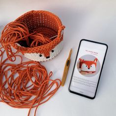 an orange and white knitted basket next to a cell phone