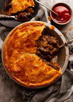 two pies with meat and sauce on the side, one is cut in half