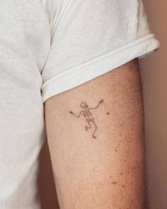 a person with a small skeleton tattoo on their left arm and the other arm behind him