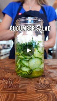 cucumber salad in a glass jar on a wooden table with a woman behind it