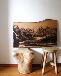 two stools sitting next to a piece of wood with mountains on the wall behind it