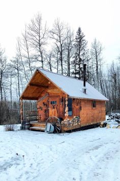 a small wooden cabin in the snow with a wagon and water wheel on the porch