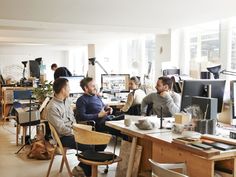 people sitting at desks in an office with computers and other items on the table