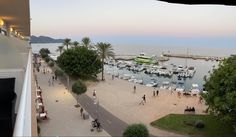 people are walking on the beach next to boats in the water at sunset or dawn