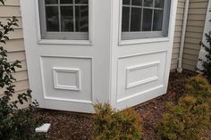 a white door with two windows on the side of a house next to shrubbery