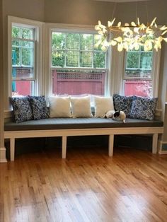 a living room with wood floors and large windows in the corner, along with a bench that has several pillows on it