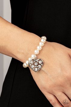 a close up of a person wearing a bracelet with pearls and a heart on it