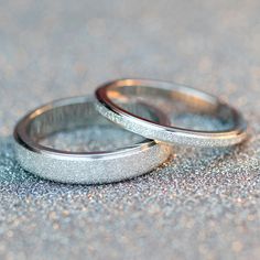 two silver wedding rings sitting on top of a glitter covered ground with sparkle in the background