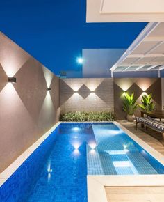 an outdoor swimming pool at night with lights on the wall and furniture in the foreground