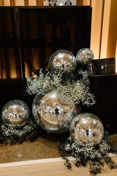 some silver balls are sitting on the floor next to a mirror ball vase with baby's breath flowers in it