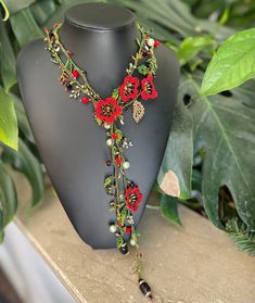 a necklace with red flowers and beads on a mannequin next to green leaves