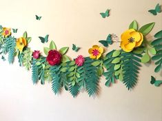 paper flowers and leaves are hanging on the wall with butterflies flying around them in the background