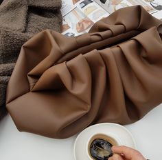 a woman is holding a coffee cup in front of a brown purse on a table