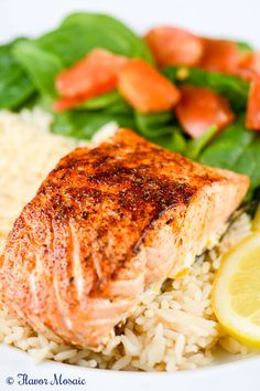 a white plate topped with salmon and rice next to lemon wedges on top of spinach