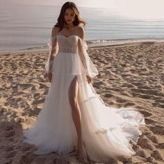 a woman standing on top of a sandy beach next to the ocean wearing a white dress