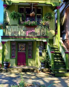 a green two story house with red door and stairs leading up to the second floor