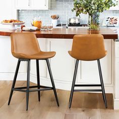 two brown leather stools sitting in front of a kitchen counter with flowers on it