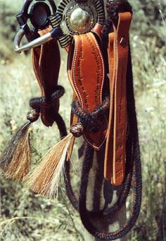 a horse saddle hanging from a rope in the grass with other items attached to it