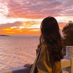 a woman is looking out at the water from a balcony overlooking an ocean and sunset