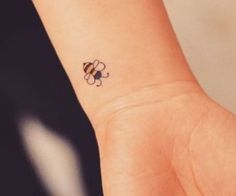 a small tattoo on the wrist of a person with a bee on it's arm