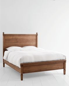 a wooden bed frame with white sheets and pillows on top of it, in an empty room