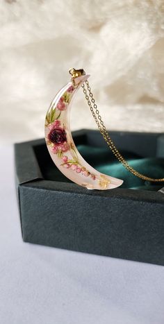 a necklace with a flowered crescent on it in a black box, sitting on a white surface