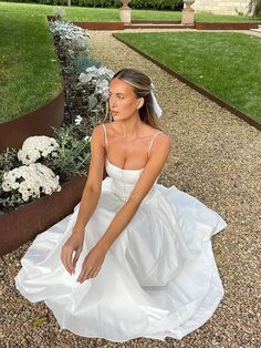 a woman in a white dress sitting on the ground next to some flowers and plants