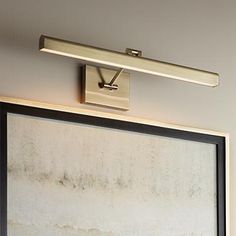 a bathroom mirror with a light on above it and a painting hanging from the wall