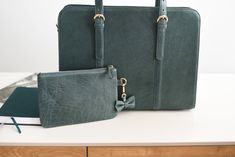 two green purses sitting next to each other on a white table with a book