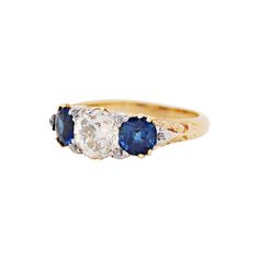 Hand carved Late Victorian three stone ring set with a 1.41ct old cut diamond and two beautiful blue sapphires on either side with a combined weight of 1.61ct all in open back, claw settings. The centre stone is decorated with four old cut diamonds on each claw. The ring is then finished with a further two old cut diamonds in white metal on either side of the sapphires, all set on top of a beautifully intricate scroll design yellow gold mount. Stamped 18. UK finger size 'J'. Three Stone Ring Settings, Bezel Set Diamond Ring, Sapphire Diamond Pendant, Antique Blue, Three Stone Ring, Bezel Set Diamond, Sapphire Pendant, Modern Ring, Pendant Rings