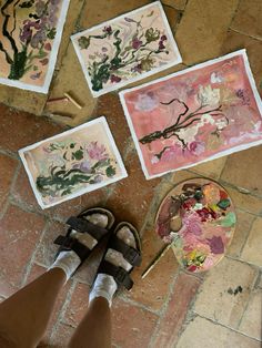 someone is standing on the floor with their feet in front of some paintings and scissors