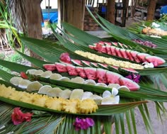 several trays filled with different types of food on top of palm leaves and flowers