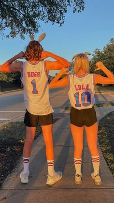 two girls in basketball uniforms are standing on the sidewalk with their arms around each other