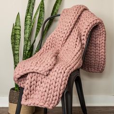 a pink knitted blanket sitting on top of a chair next to a potted plant