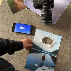 a person holding a cell phone in front of a camera and some pictures on the ground