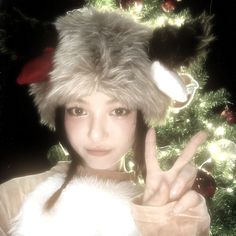 a woman wearing a fur hat making the peace sign with her hand in front of a christmas tree