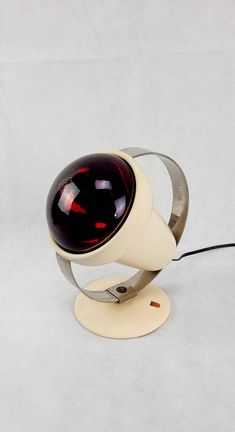 a red and white lamp sitting on top of a wooden table next to a black cord