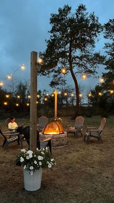 an outdoor fire pit surrounded by chairs and string lights