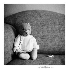 a black and white photo of a teddy bear sitting on a couch