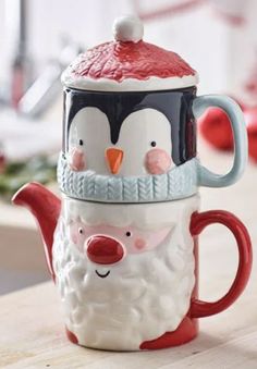 two penguin mugs sitting on top of a wooden table next to each other, one wearing a santa claus hat