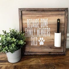 a wooden sign sitting on top of a table next to a potted plant and toilet paper dispenser