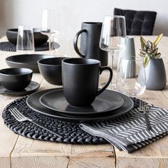 a wooden table topped with black plates and cups on top of eachother's placemats